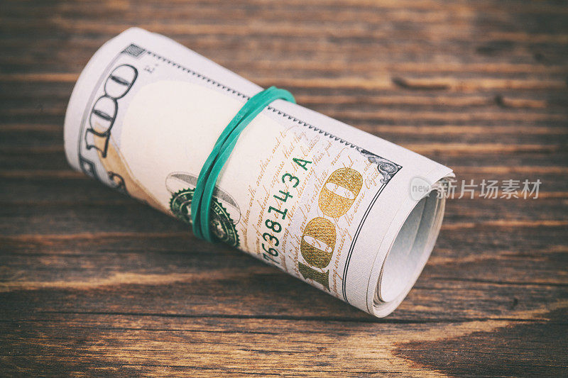 Roll of one hundred dollar bills on wooden rustic table